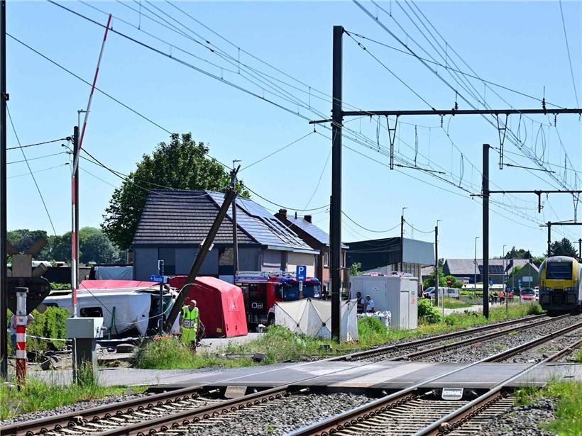 Zug und Schulbus kollidieren bei Unfall in Belgien, Unfallstelle mit Einsatzkräften und beschädigten Fahrzeugen