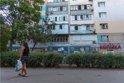 In Odessa läuft eine Frau mit Einkaufstaschen an einem durch russische Luftangriffe beschädigten Wohngebäude vorbei
