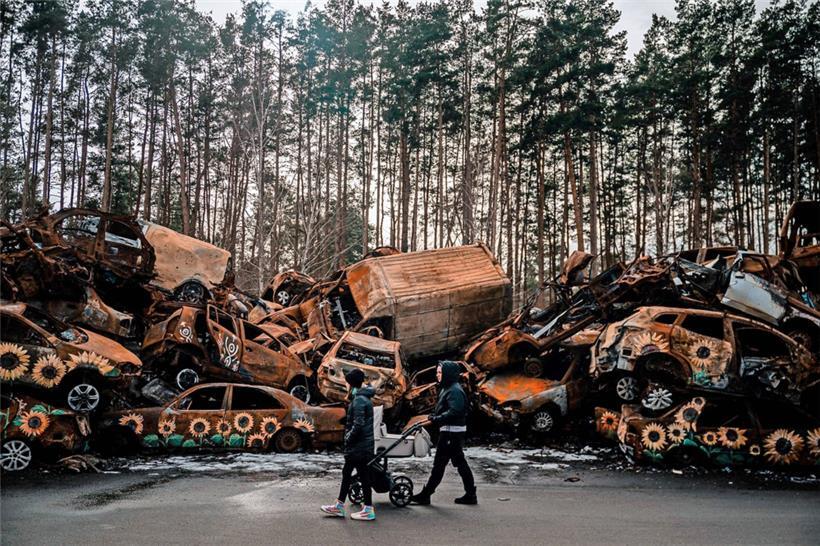 In der ukrainischen Stadt Irpin, nahe Kiew, geht eine Frau mit einem Kinderwagen an einem Haufen während der russischen Besatzung zerstörter Fahrzeuge vorbei
