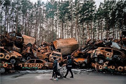 In der ukrainischen Stadt Irpin, nahe Kiew, geht eine Frau mit einem Kinderwagen an einem Haufen während der russischen Besatzung zerstörter Fahrzeuge vorbei
