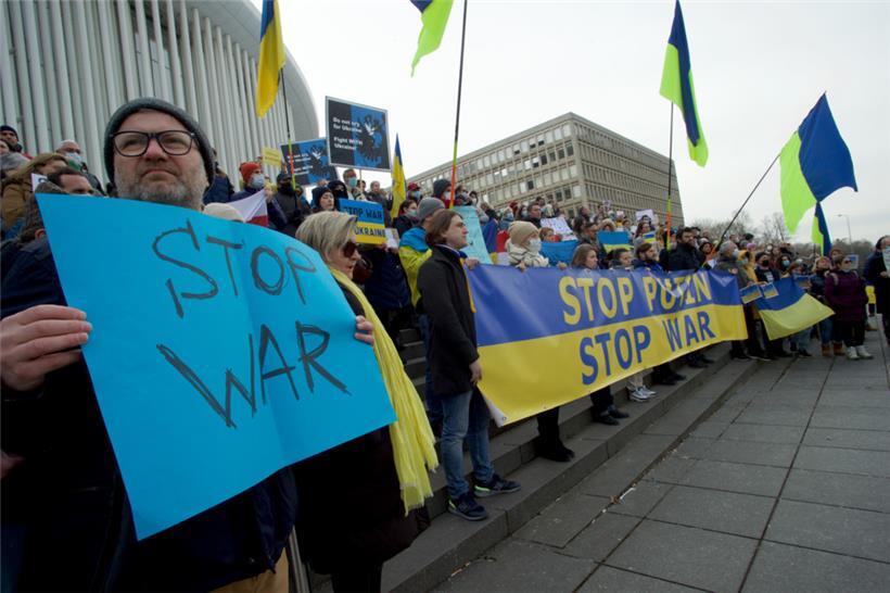 In die Farben Blau sowie Gelb gehüllt und mit Plakaten in ihrer Hand, fordern die Protestler, dass Russland den Angriff auf die Ukraine beendet

