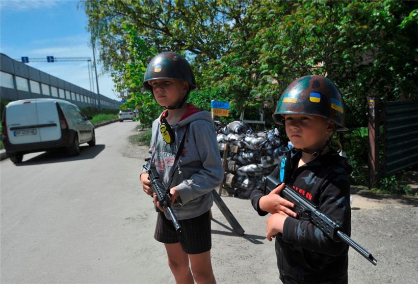 In einem Dorf nahe Kiew spielen ukrainische Kinder als Kämpfer der Territorialverteidigung verkleidet einen Checkpoint nach
