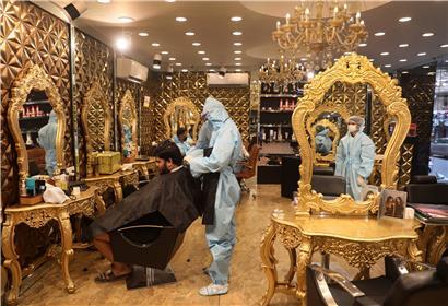 Indien, Neu Delhi: Ein Friseur in einem Schutzanzug betreut einen Salon-Kunden. 
