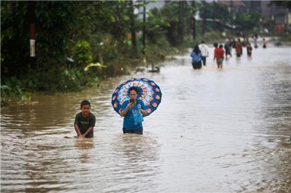 Indonesien, Medan: Menschen waten durch das Wasser einer überfluteten Straße
