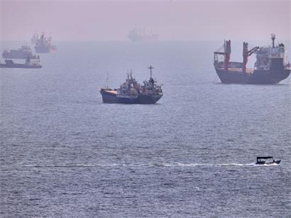 Iran, Bandar Abbas: Ein kleines Boot segelt an Frachtschiffen und anderen Handelsschiffen vorbei, die in der Straße von Hormus vor Bandar Abbas im Iran vor Anker liegen