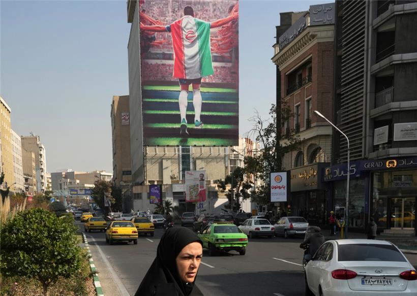 Iran, Teheran: Ein staatlich gesponsertes Plakat, das einen Fußballspieler mit der Nationalflagge beim Einlaufen in ein Stadion zeigt, hängt an einem Gebäude. Die Fußball-Nationalspieler von Iran nehmen an der Fußball-WM 2022 in Katar teil. Seit dem Tod der iranischen Kurdin Amini Mitte September gibt es anhaltende landesweite systemkritische Proteste im Iran.
