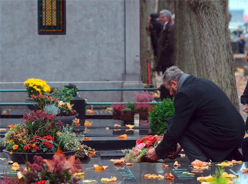 Jemand legt auf dem Ettelbrücker Friedhof zu Allerheiligen im Jahr 2019 einen Blumenkranz an einem Grab nieder
