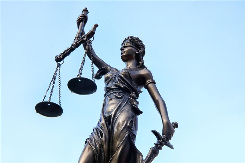 Justitia-Statue mit Waage und Schwert, Symbol für Gerechtigkeit und Rechtsprechung vor blauem Hintergrund