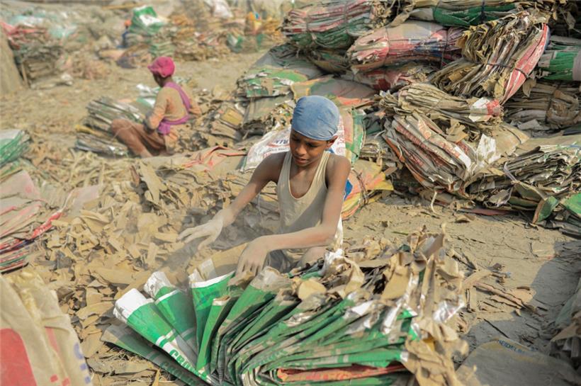 Kinder sortieren inmitten von Zementstaub gebrauchte Zementsäcke am Ufer des Surma-Flusses in Sylhet, Bangladesch
