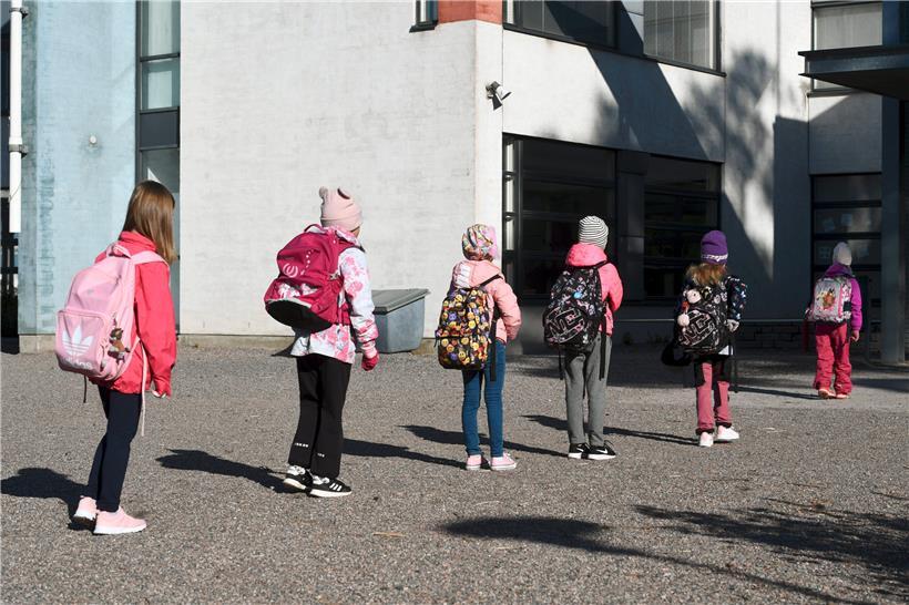 Kinder stehen unter Einhaltung des Mindestabstands vor dem Eingang einer Schule
