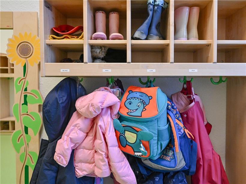 Kinderkleidung hängt zum Trocknen in einer Kita-Garderobe, bunte Jacken und Mützen sichtbar