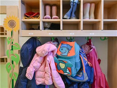 Kinderkleidung hängt zum Trocknen in einer Kita-Garderobe, bunte Jacken und Mützen sichtbar