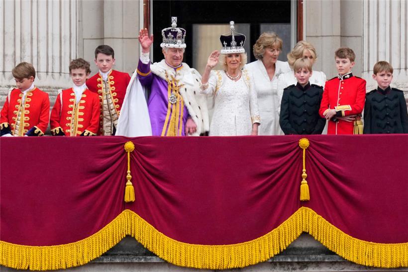 König Charles III. (M,l) und Königin Camilla (M,r) winken nach ihrer Krönungszeremonie vom Balkon des Buckingham Palastes aus der Menge zu

