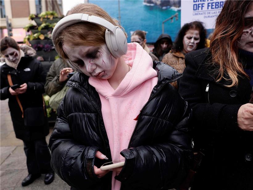 Zombies mit realistischer Maske starren auf Smartphones bei Horror-Happening in Madrid auf belebter Straße
