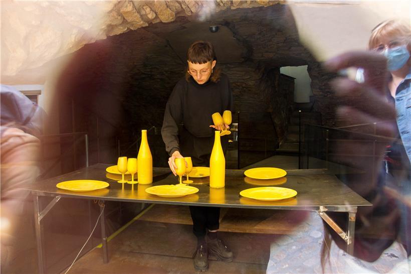Mahé Cabel installant „A nos mères“, la vaisselle en cires d’abeilles posée sur une table chauffante
