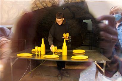 Mahé Cabel installant „A nos mères“, la vaisselle en cires d’abeilles posée sur une table chauffante
