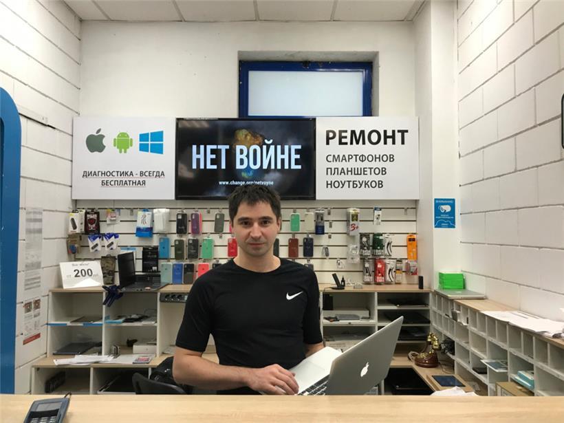 Marat Gratschew, Leiter eines Geschäfts, das Apple-Geräte repariert, steht vor einem Schild in russischer Sprache mit der Aufschrift „Nein zum Krieg“. Er wurde denunziert und im Rahmen einer offiziellen Niederschlagung der Proteste wegen Verunglimpfung des Militärs angeklagt. 

