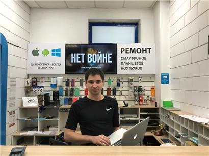Marat Gratschew, Leiter eines Geschäfts, das Apple-Geräte repariert, steht vor einem Schild in russischer Sprache mit der Aufschrift „Nein zum Krieg“. Er wurde denunziert und im Rahmen einer offiziellen Niederschlagung der Proteste wegen Verunglimpfung des Militärs angeklagt. 
