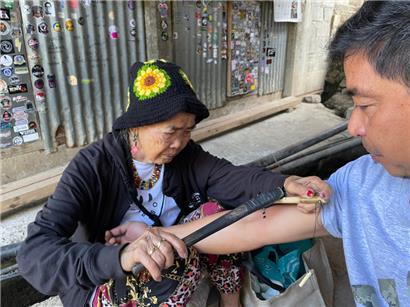Maria Oggay, im Volksmund als Apo Whang-Od bekannt, die älteste Mambabatok oder traditionelle Tätowiererin der Philippinen, tätowiert einen Mann mit traditioneller Technik am Arm 
