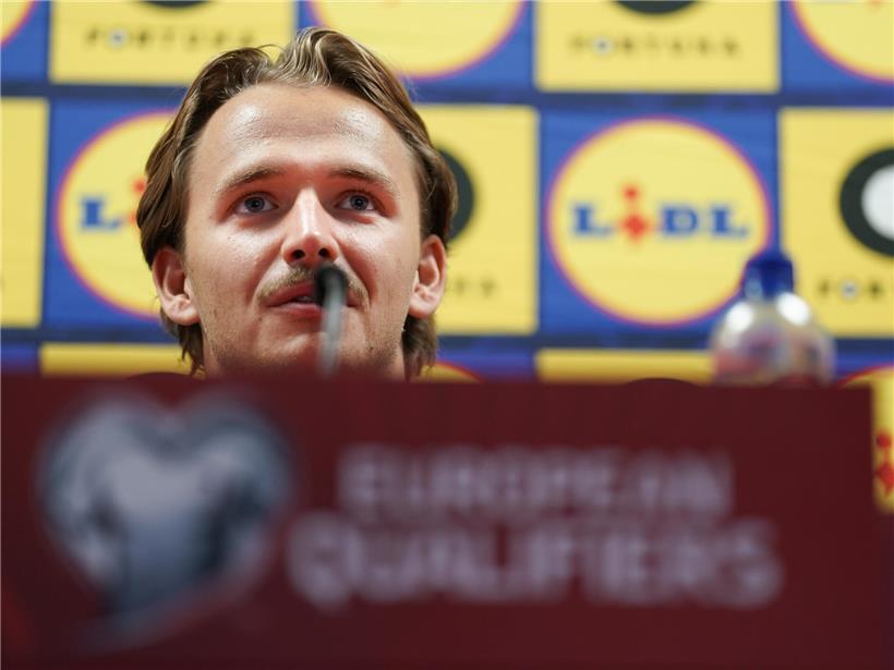 Porträt von Mathias Olesen, professioneller Fußballspieler in Sportkleidung, lächelnd vor neutralem Hintergrund