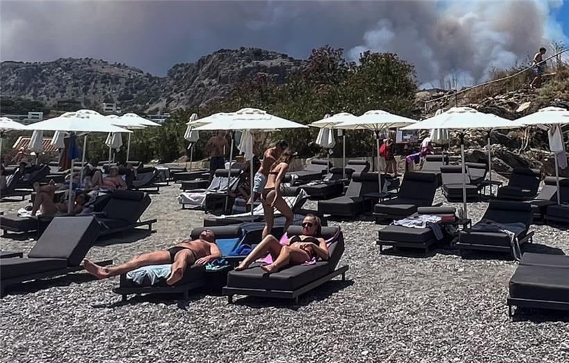 Menschen beim Sonnenbaden am Viglika Beach in Lindos – im Hintergrund steigt Rauch von den Bränden auf
