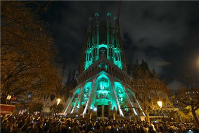 Menschen beobachten eine Lichtshow, die an die Fassade der Sagrada Familia Basilika des spanischen Architekten Antoni Gaudi projiziert wird und den Beginn der Karwoche in Barcelona am 14. April 2025 markiert
