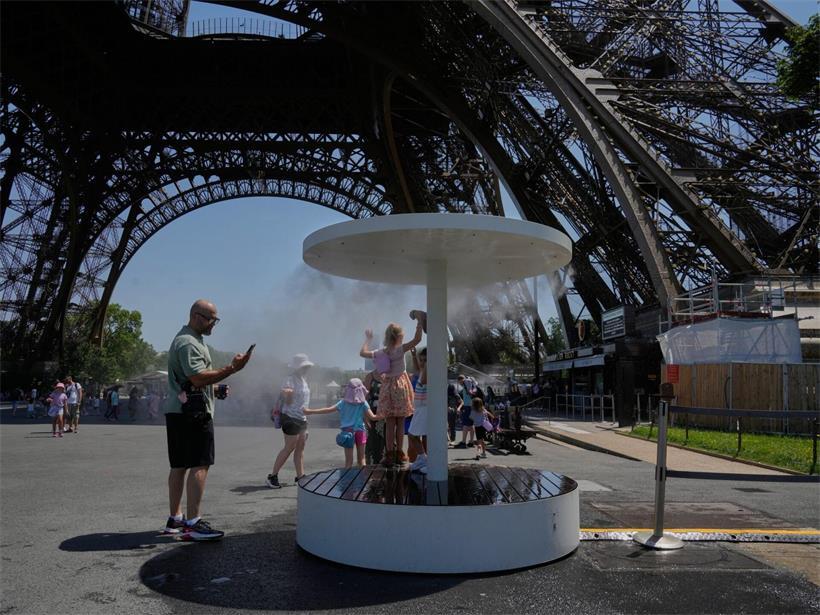 Menschen kühlen sich im Wassersprühnebel am Eiffelturm an einem sonnigen Sommertag in Paris