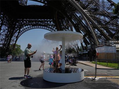 Menschen kühlen sich im Wassersprühnebel am Eiffelturm an einem sonnigen Sommertag in Paris