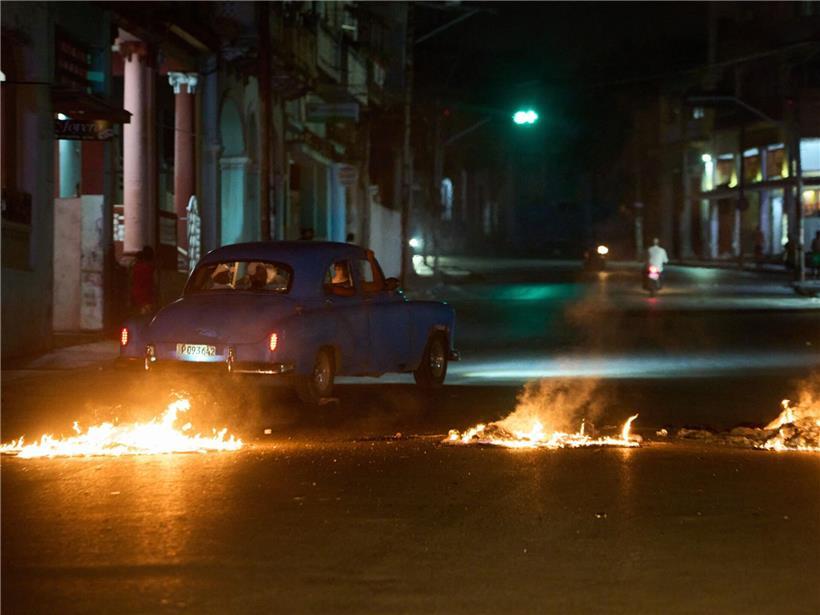 Menschen in amerikanischem Oldtimer fahren durch Barrikade von Anwohnern bei Protest gegen Stromausfälle in Havanna
