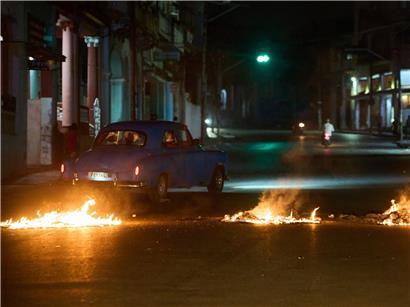 Menschen in amerikanischem Oldtimer fahren durch Barrikade von Anwohnern bei Protest gegen Stromausfälle in Havanna