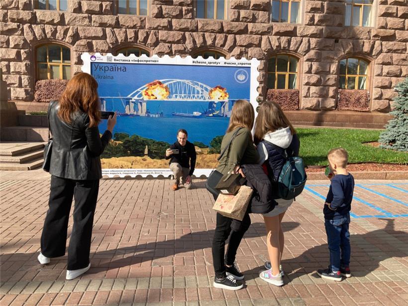 Menschen fotografieren sich in Kiew vor einem Plakat, das Explosionen auf der für Russland wichtigen Krim-Brücke zeigt
