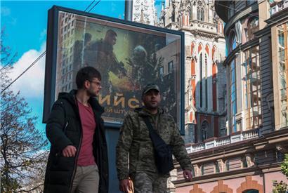 Menschen gehen in Kiew an einem Plakat vorbei, auf dem ukrainische Soldaten abgebildet sind, die mit Bösewichten kämpfen. Die Aufschrift fordert auf: „Kämpft gemeinsam in der 3. Angriffsbrigade“ (eine Brigade der ukrainischen Bodentruppen)
