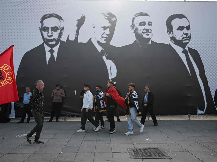 Menschen gehen in Pristina an einem großen Transparent mit den Führern der Kosovo-Befreiungsarmee vorbei