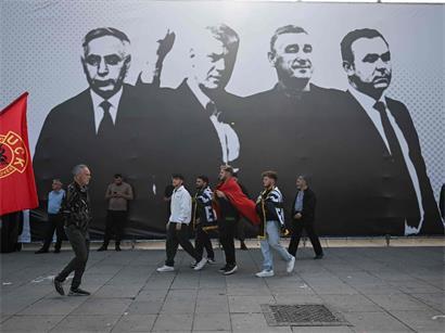 Menschen gehen in Pristina an einem großen Transparent mit den Führern der Kosovo-Befreiungsarmee vorbei