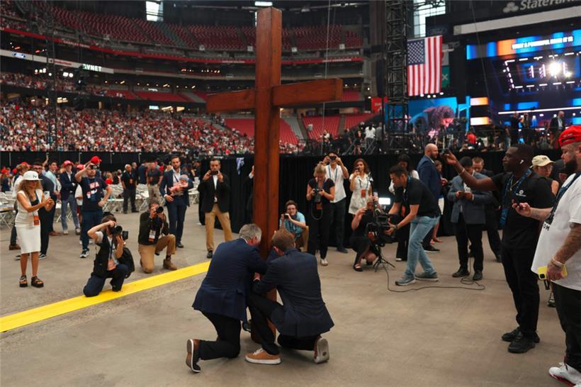 Menschen knien vor einem großen Kreuz vor der öffentlichen Gedenkfeier