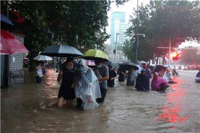 Menschen waten in der zentralchinesischen Provinz Henan durch eine überflutete Straße
