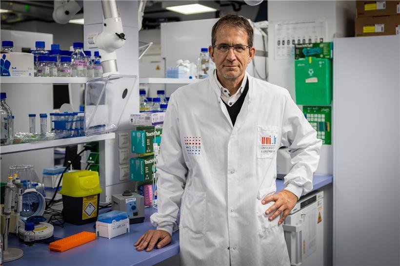 Michael Heneka, Direktor des Luxembourg Centre for Systems Biomedicine (LCSB), porträt im Büro vor wissenschaftlichem Hintergrund