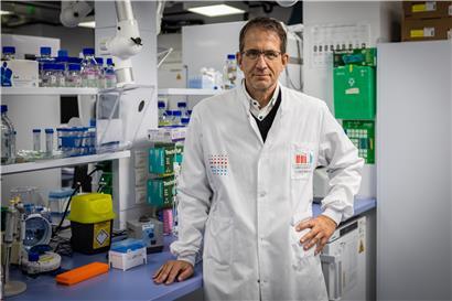 Michael Heneka, Direktor des Luxembourg Centre for Systems Biomedicine (LCSB), porträt im Büro vor wissenschaftlichem Hintergrund