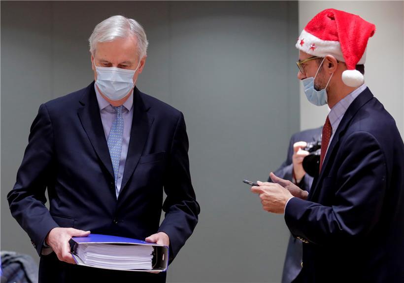 Michel Barnier (l), EU-Chefunterhändler für den Brexit aus Frankreich, trägt einen Ordner mit dem Brexit-Handelsabkommen neben einem Kollegen, der eine Weihnachtsmannmütze trägt, während einer Sondersitzung im EU-Hauptquatier
