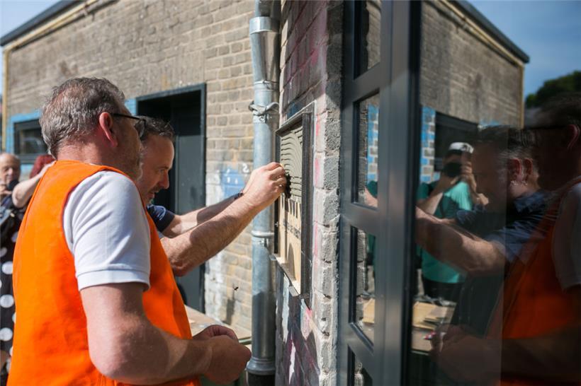 Mit großer Sorgfalt werden die ersten Fliesen mit dem Namen des Projekts angebracht
