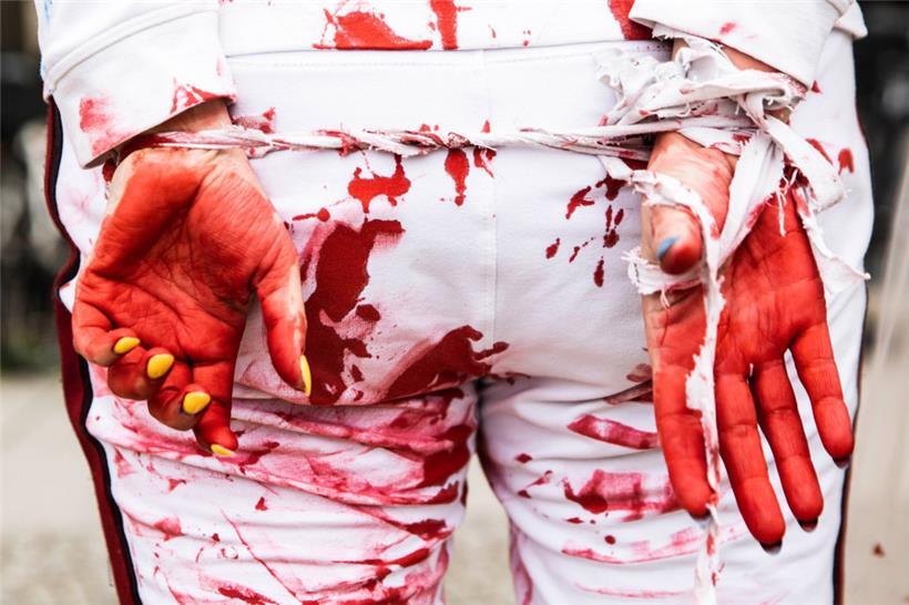 Mit verbundenen Händen und Kunstblut demonstriert eine Frau gegen sexualisierte Gewalt im russischen Angriffskrieg auf die Ukraine
