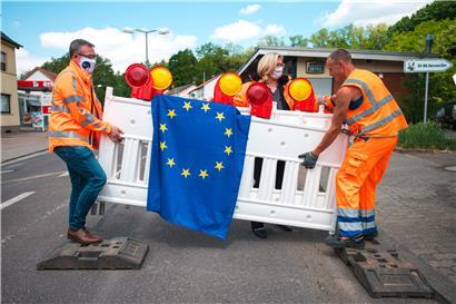 Mitarbeiter des Landesbetriebs für Straßenbau bauen unter Mithilfe von Anke Rehlinger, Ministerin für Wirtschaft, Arbeit, Energie und Verkehr und stellvertretende Ministerpräsidentin des Saarlands, die Absperrbaken am Grenzübergang ab – ein Bild aus besseren Zeiten
