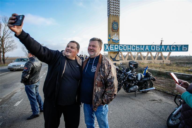 Motorradfahrer machen Selfies vor einem Straßenschild mit der Aufschrift „Cherson Oblast“ 
