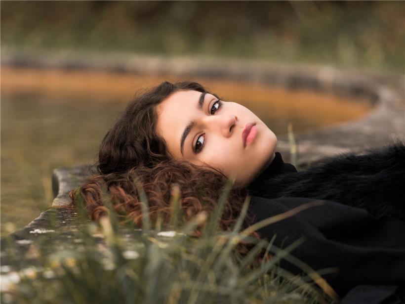 Porträt von Naomi Ayé mit natürlichem Make-up und lockigem Haar, Musikerin und Songwriterin in entspannter Pose