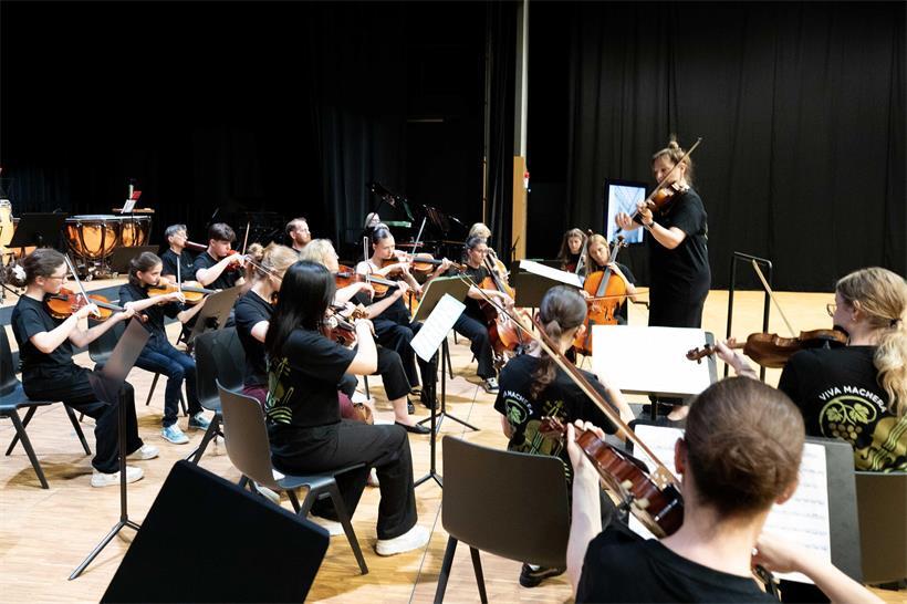 Orchesterprobe mit Musikern, Geigen und Dirigent in einem Konzertsaal, klassische Musik live üben