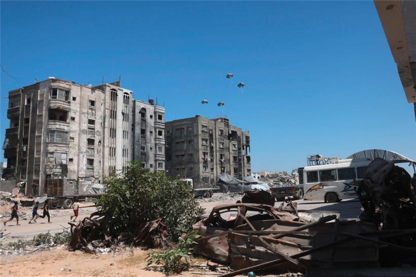 Palästinenser rennen zu Hilfspaletten, während diese nach dem Abwurf aus einem Militärflugzeug nahe Jabalia im nördlichen Gazastreifen am 20. August 2025 herabsegeln
