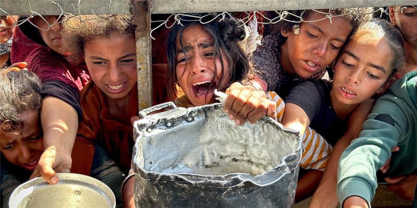 Palästinensische Kinder versuchen im Gebiet Al-Mawasi im Gazastreifen, mit ihren Töpfen Nahrungsmittel zu bekommen, die von Wohltätigkeitsorganisationen verteilt werden
