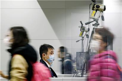 Passagiere tragen Atemschutzmasken, während sie an einem Quarantänebeamten vorbeigehen
