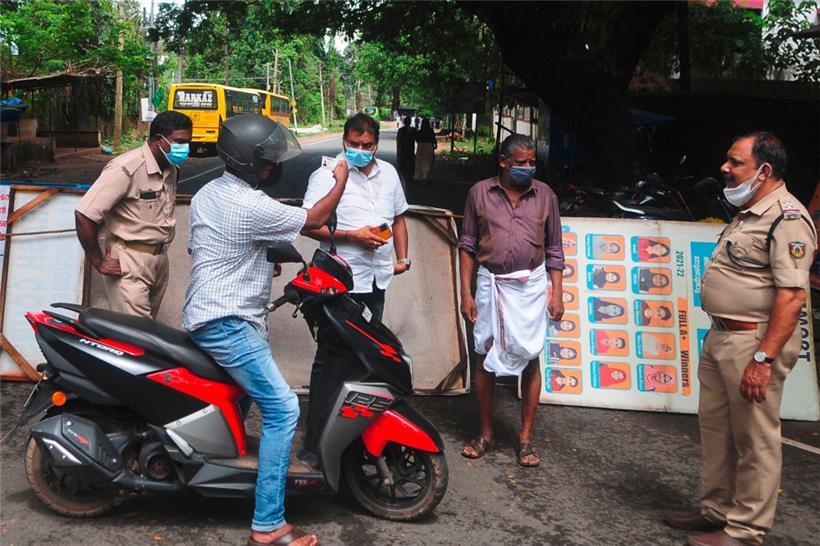 Polizei und Gesundheitsbeamte überprüfen den Ausweis eines Mannes an einem Kontrollpunkt entlang einer Straße, die in eine Sperrzone führt.
