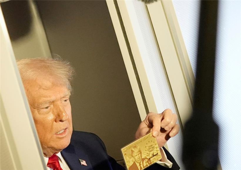 Präsident Donald Trump hält die goldene 5-Millionen-Dollar-Karte hoch, während er an Bord der Air Force One auf dem Weg nach Miami zu Reportern spricht
